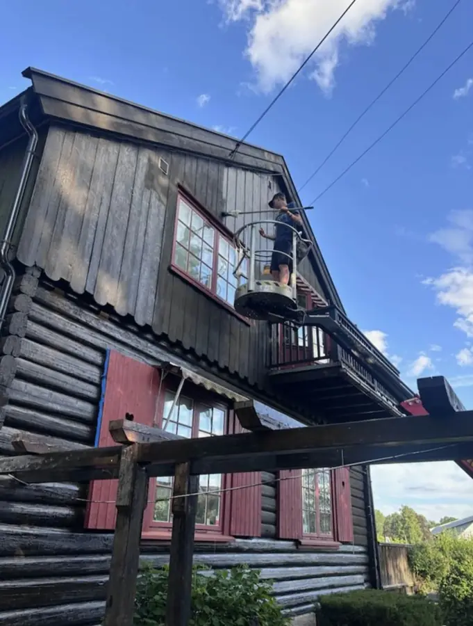 En av guttene jobber med fasaden på et tømmerhus fra en lift